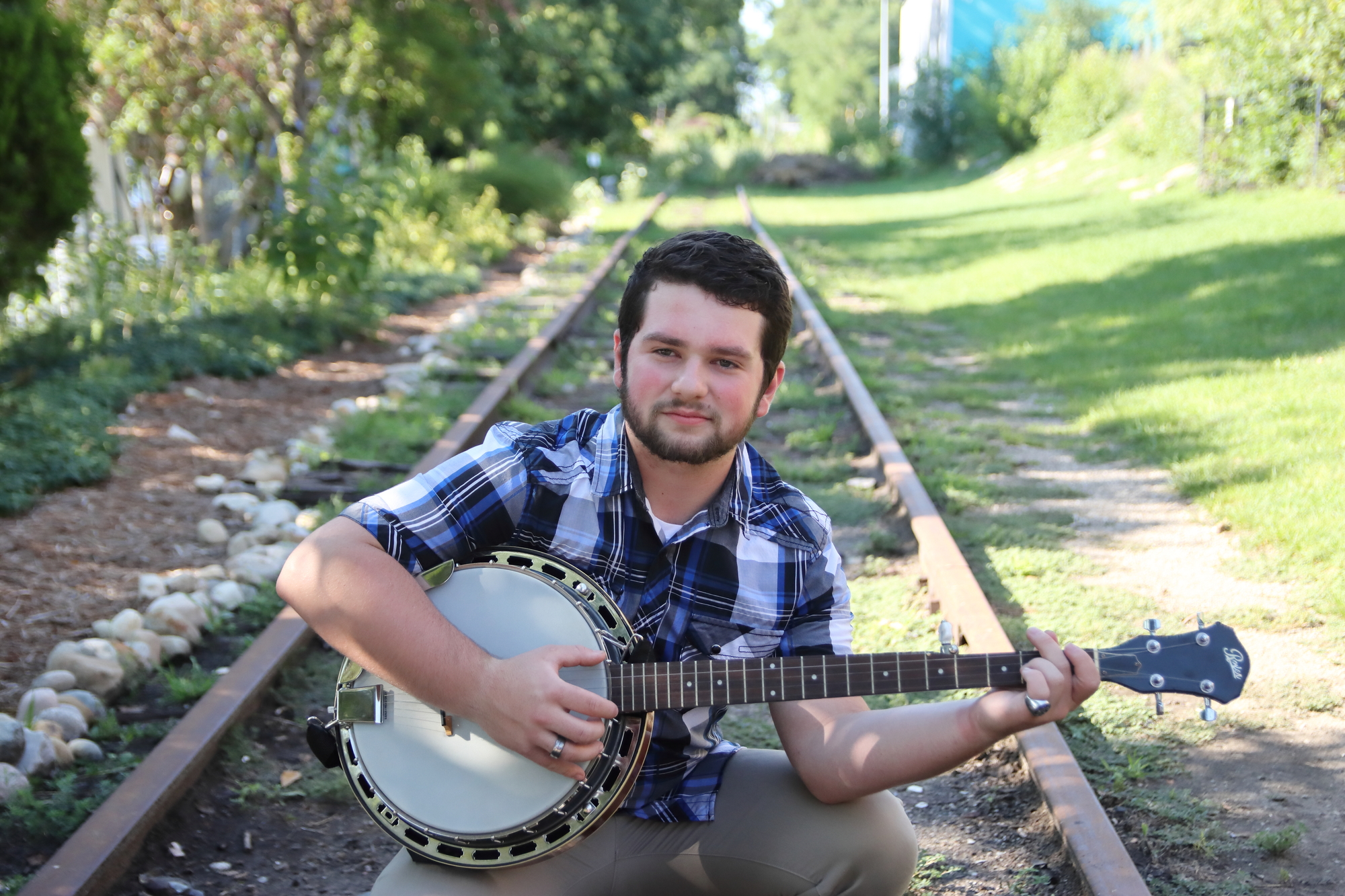 young man playing a banjo on abandoned railroad tracks
