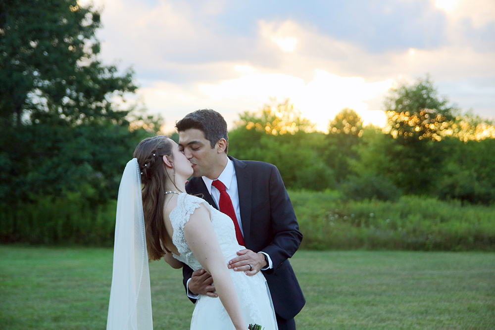 Newly married couple kissing in front of a sunset at their reception
