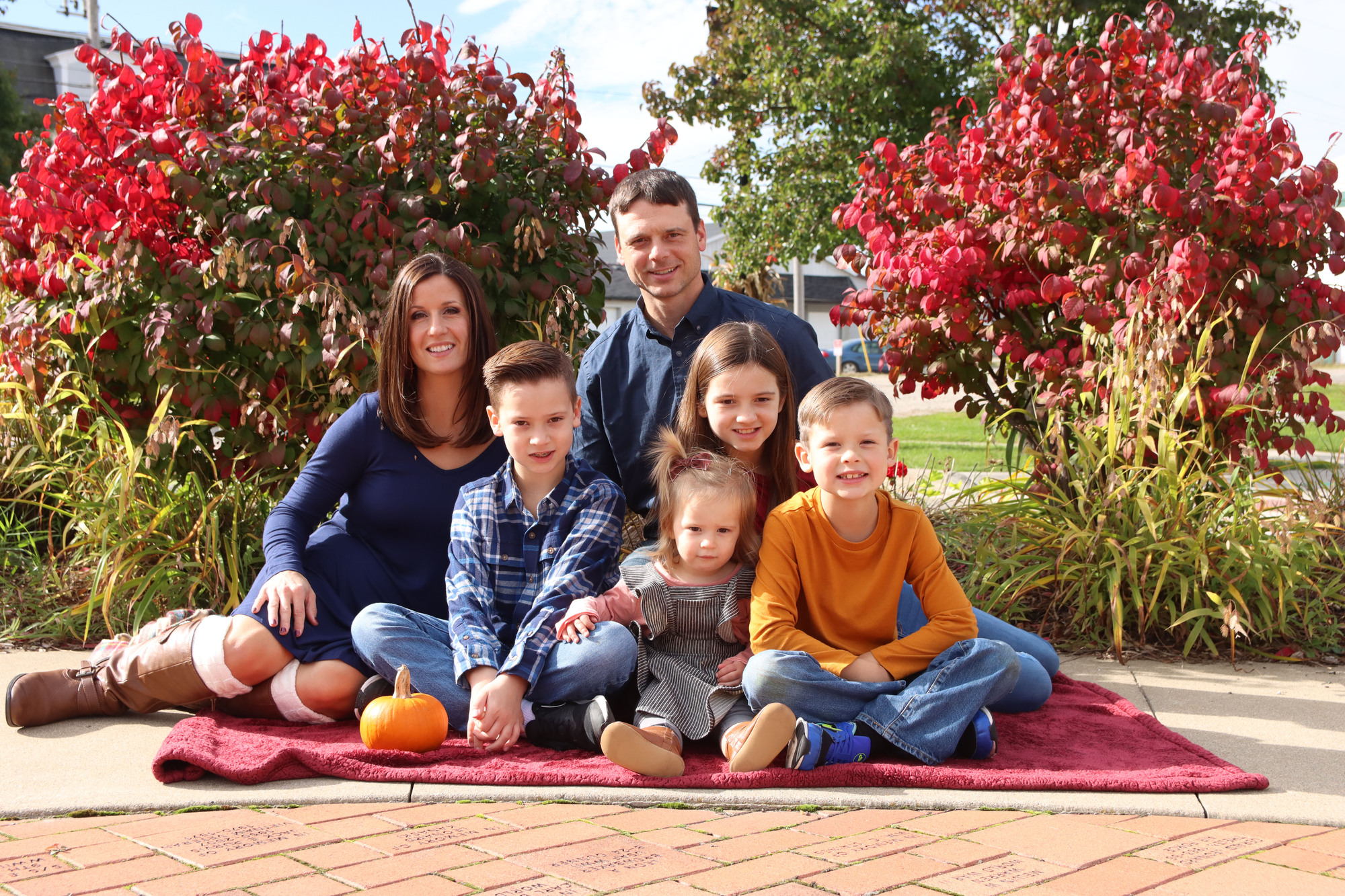 family sitting on a burgundy blanket on a landscaped area in downtown Saint Johns Michigan