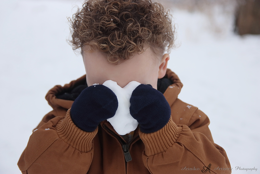 Soon to be brother hiding behind little snow heart during maternity session at Harris Nature Center in Okemos, Michigan