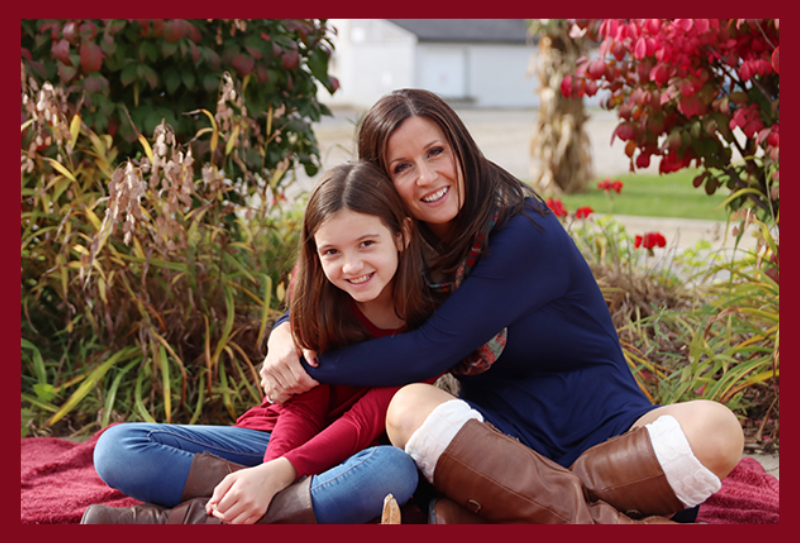 mother and daughter pose in St. John's on a blanket by colorful fall bushes.