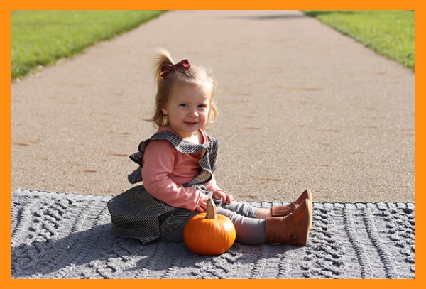 young girl poses with a mini pumpkin on a trail in St. John's Michigan