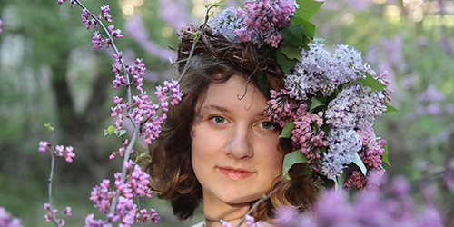 Young woman with a lilac flower crown standing near Red Bud blooming trees