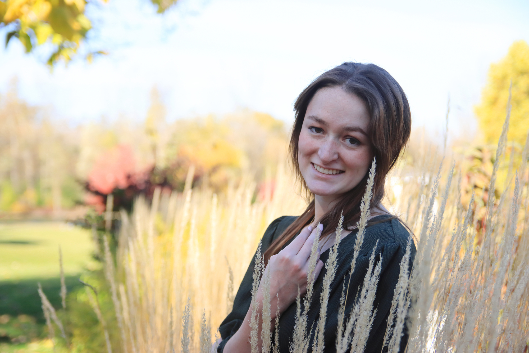 Young woman in green dress stands in tall yellow grass near a pond at Meridian Historical Village in Okemos Michigan