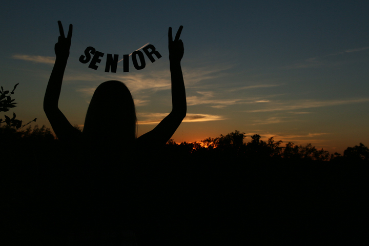 Sunset on a high hill with a senior holding the words SENIOR between her hands it is silhouetted in the fading sunlight 