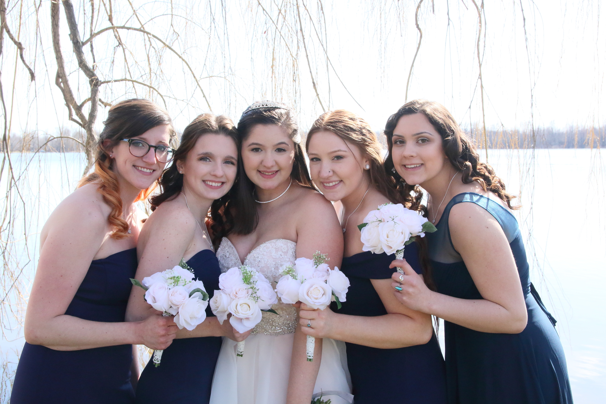 bride with her bridesmaids standing in front of a lake on a sunny day