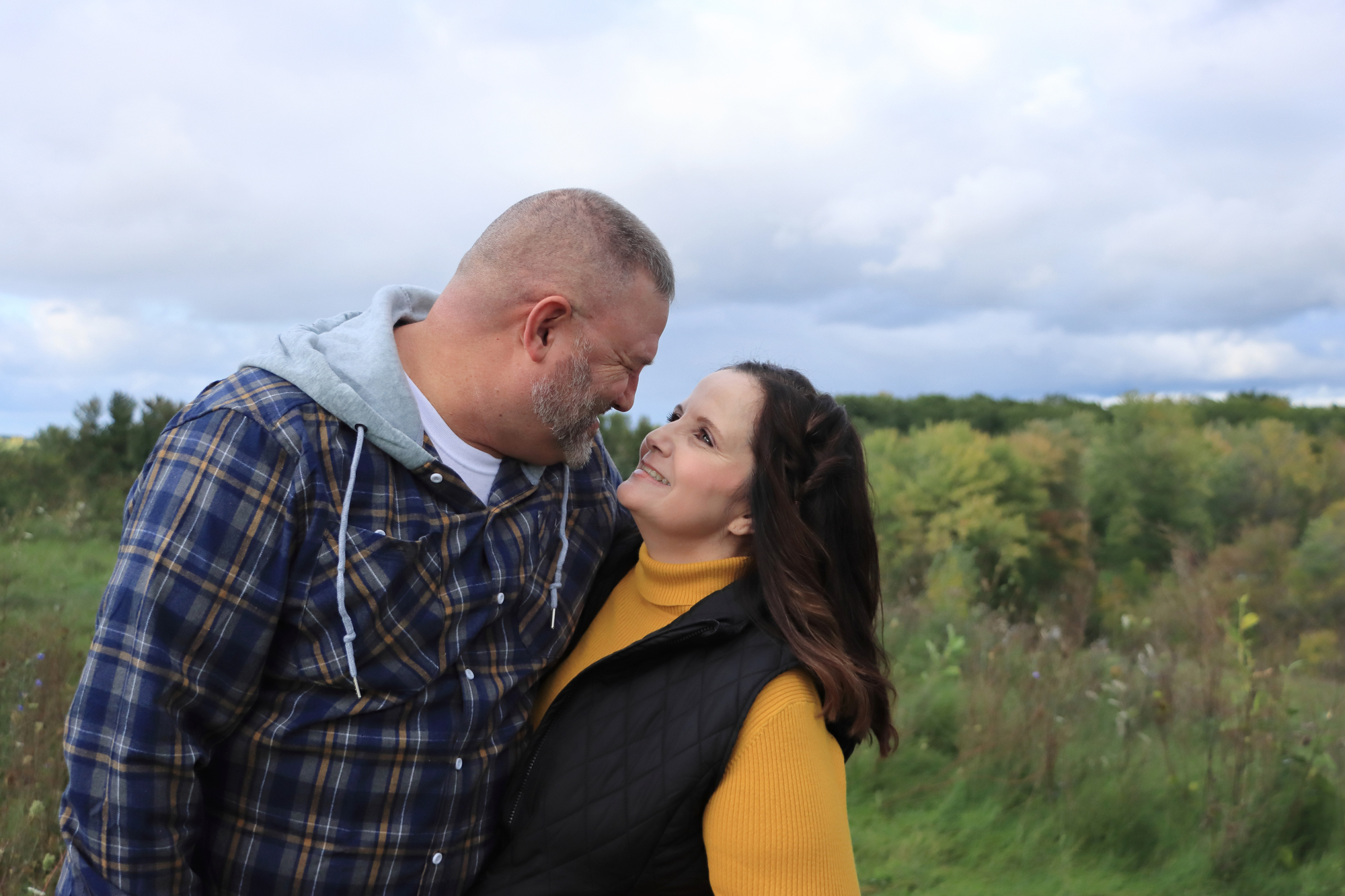 a woman wearing yellow and black looks into the eyes of her husband who has a blue flannel shirt on