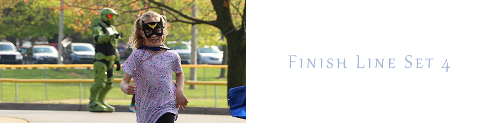 a little girl with blond hair and a batman mask smiles as she crosses the finish line