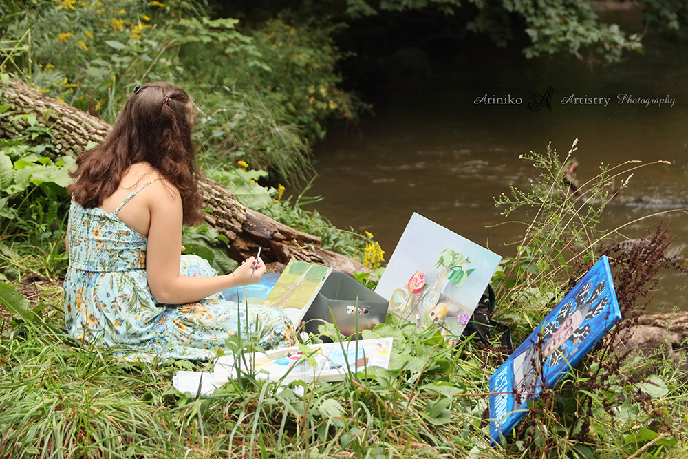 Young artist sitting with her art and painting on the banks in Charlotte, Michigan