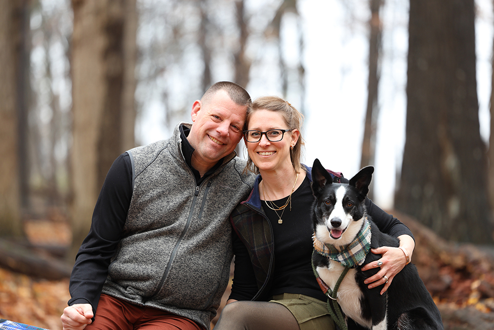 A couple and their black dog pose in a park in west Greater Lansing, Michigan