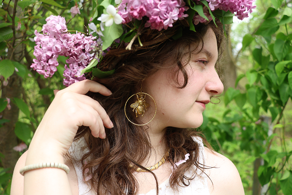A young woman wearing bumble bee earrings and a lilac flower crown